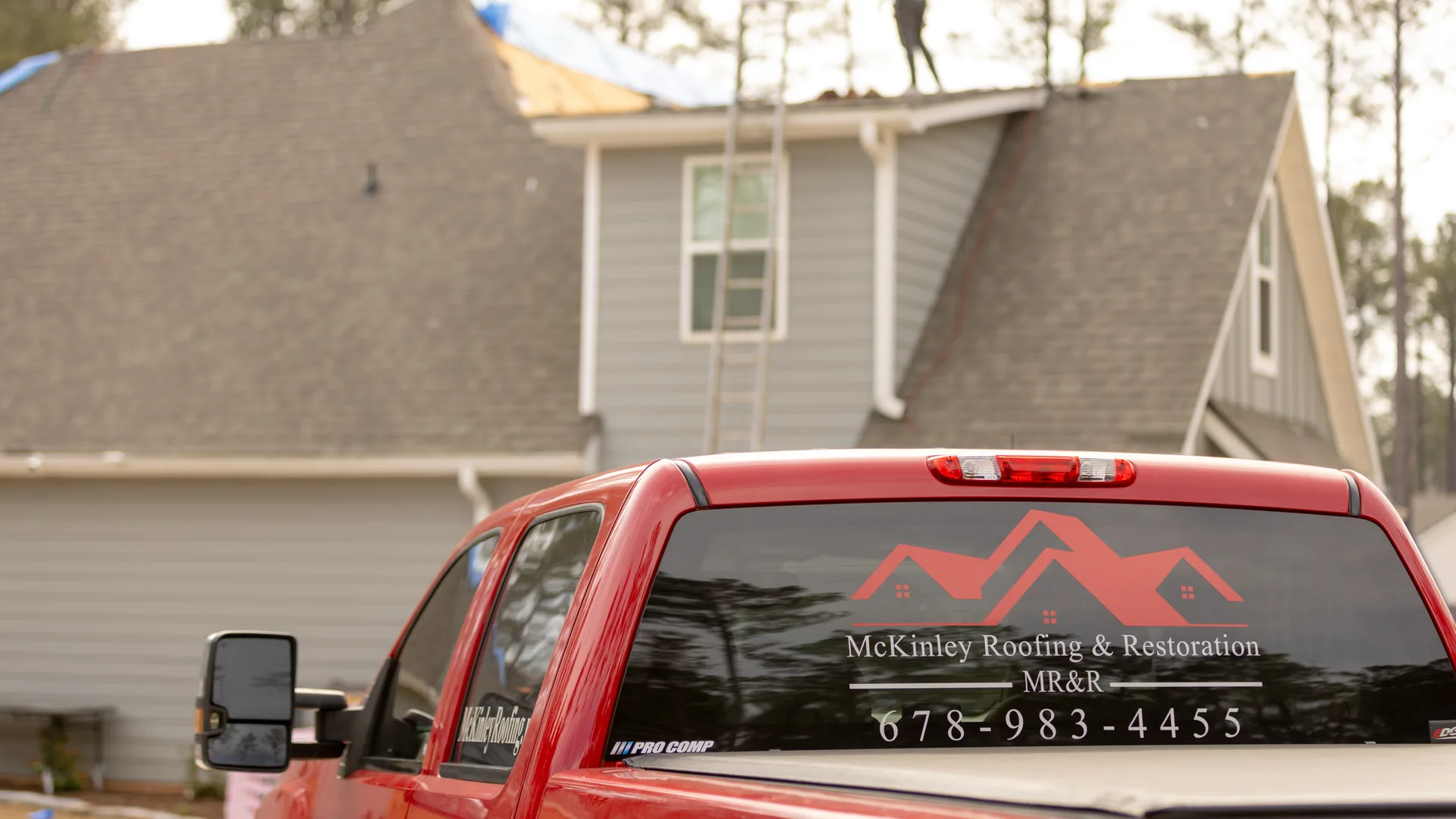 McKinley Roofing and Restoration truck parked at a two-story home while a crew member works on the roof